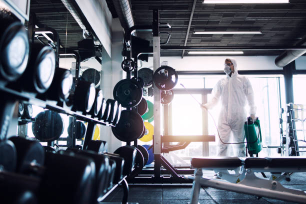 Man in PPE sanitizing gym equipment