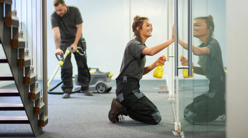 happy young lady cleaning the window and man vacuuming carpet