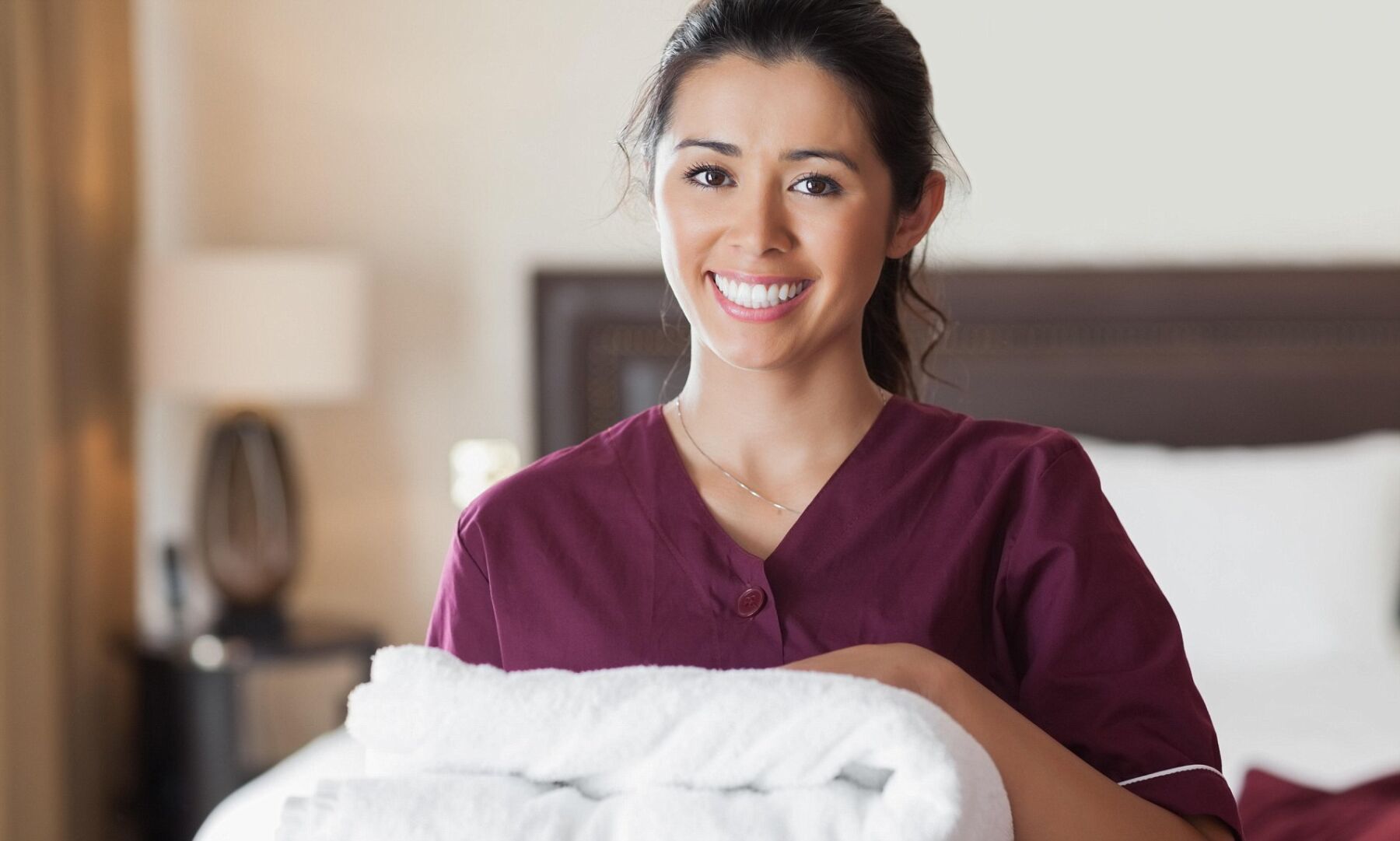 female hotel cleaner smiling while holding clean comforter