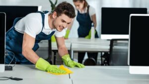 two young cleaners wiping desks with rags in office