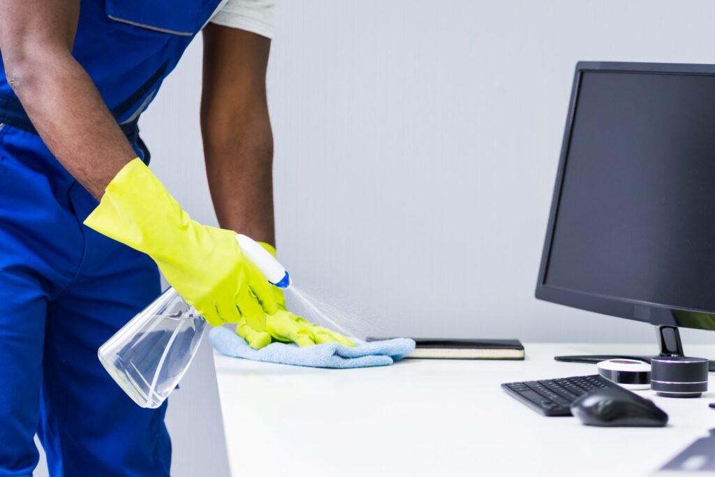 Young Male Maid Cleaning Glass Desk With Feather Duster In Office