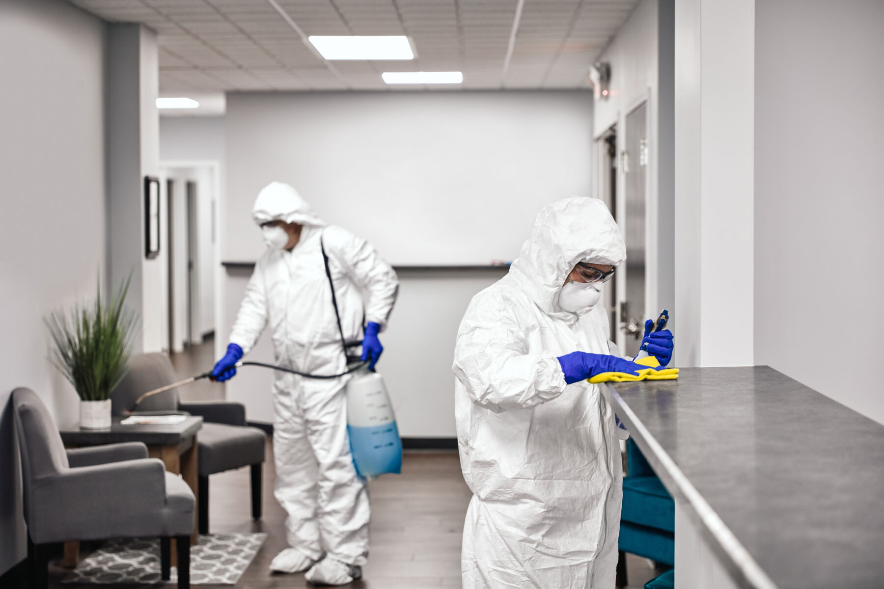 Two people in protective workwear cleaning and disinfecting offices.