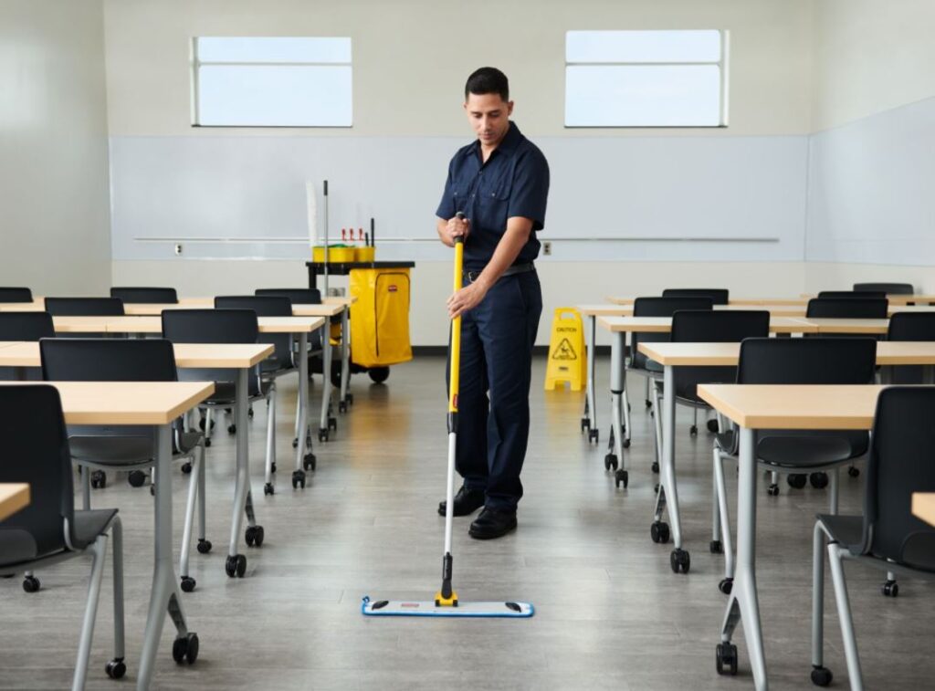 A janitorial man cleaning and mopping the floor of a classroom