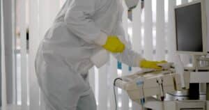 janitor in PPE doing sanitization of equipment in hospital room.