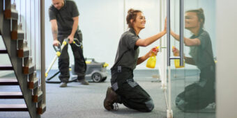 happy young lady cleaning the window and man vacuuming carpet