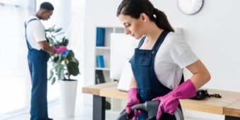 a man cleaning the plants and a woman vaccuming the office floor