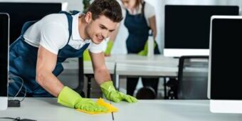 two young cleaners wiping desks with rags in office