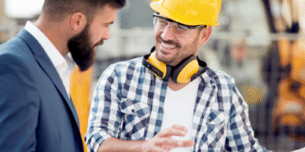 two man talking in a construction site with project plan in their hands